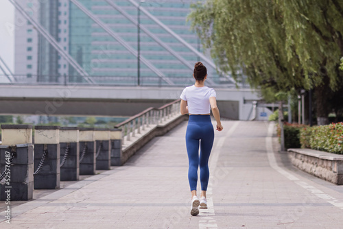 Young brunette Woman running on asphalt road in summer park. Active sporty caucasian female has morning workout. Athletic person in sportswear exercises outdoor. Dressed leggings and sportive top © Алина Бузунова