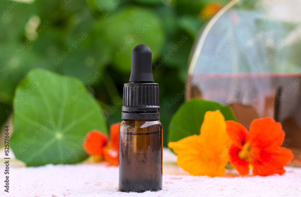 Homemade tincture (elixir) of nasturtium in a dropper. In the distance, a bottle of a ready-made, slightly orange tincture. The whole is decorated with fresh flowers. Shallow depth of field. Homemade tincture (elixir) of nasturtium in a dropper. In the distance, a bottle of a ready-made, slightly orange tincture. The whole is decorated with fresh flowers. Shallow depth of field.