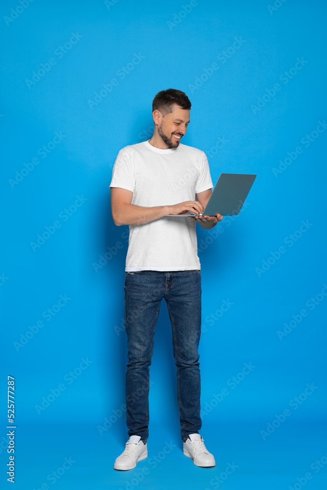 Happy man looking at laptop on light blue background Happy man looking at laptop on light blue background
