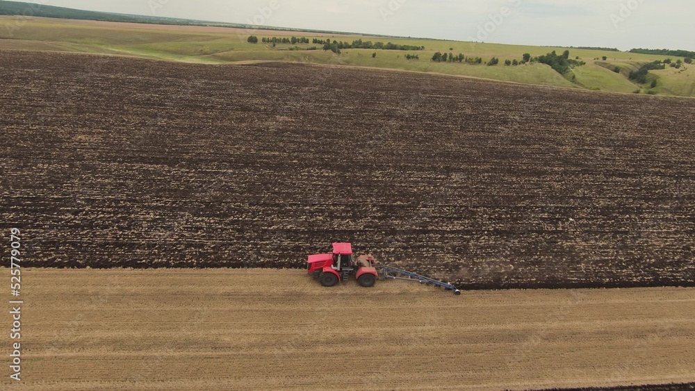 agriculture. tractor plows the soil. industry business agriculture concept. aerial drone video. red tractor machine plows the land with a large plow turns over pieces of farm dirt