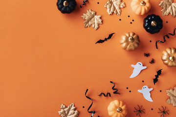 Halloween holiday frame with party decorations of pumpkins, bats, ghosts, spiders on golden background top view. Happy halloween card in flat lay style.