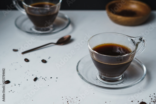 Contemporary style coffee food and drink photo. Set against a white background. Black coffee in glass cup and saucer. 