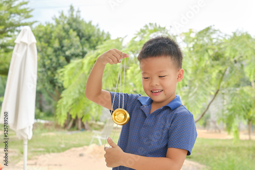 Cute little Asian boy having fun learning how to play with a yo-yo skill toy alone at home backyard