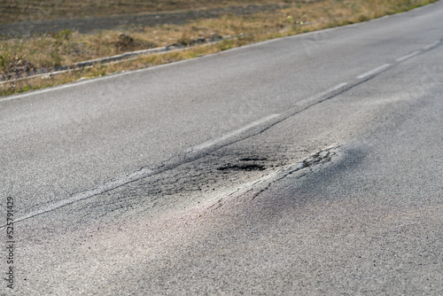Broken road with holes and cracks built in countryside on hot sunny day. Deformed and expanded asphalt surface with potholes caused by heavy overloaded trucks driving on highway at rural site closeup