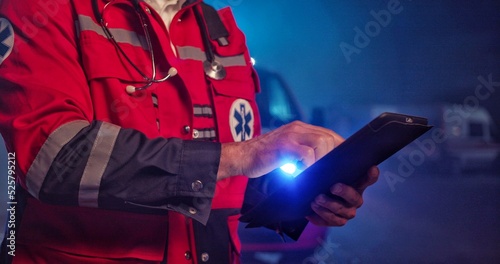 Close up hands paramedic doctor in uniform holding a digital tablet. Ambulance car on background.
