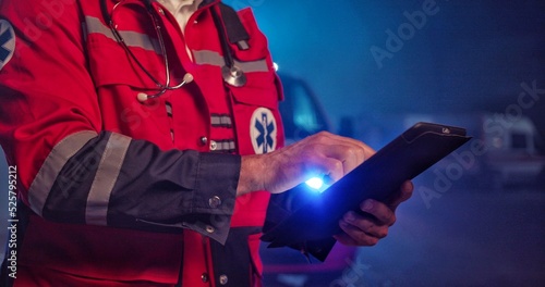 Close up hands paramedic doctor in uniform holding a digital tablet. Ambulance car on background. photo
