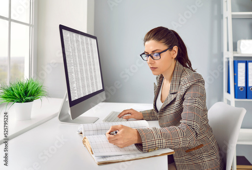 Print op canvas Concentrated female accountant compares data in spreadsheet and in paper ledger