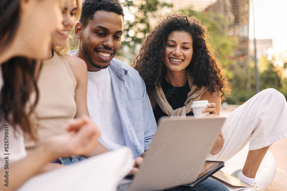 Nice young interracial students team work on laptop sitting outdoors. Guy and girls use modern technologies. Leisure concept Nice young interracial students team work on laptop sitting outdoors. Guy and girls use modern technologies. Leisure concept