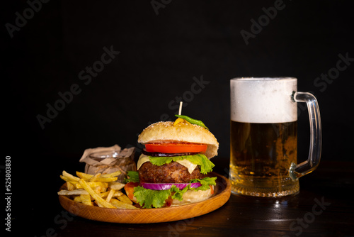 tasty hamburger burger sandwich with french fries and ketchup on a wooden tray a glass of cool beer with foam fast food black background