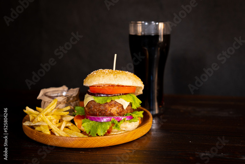 Delicious hamburger with cola and potato fries on a wooden table with a dark brown background behind. Fast food concept.