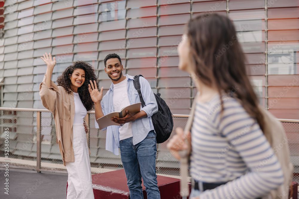 Positive young african guy and girl greet girlfriend spending time  outdoors. Brunette students wear casual clothes in spring. Real emotions  concept Stock Photo