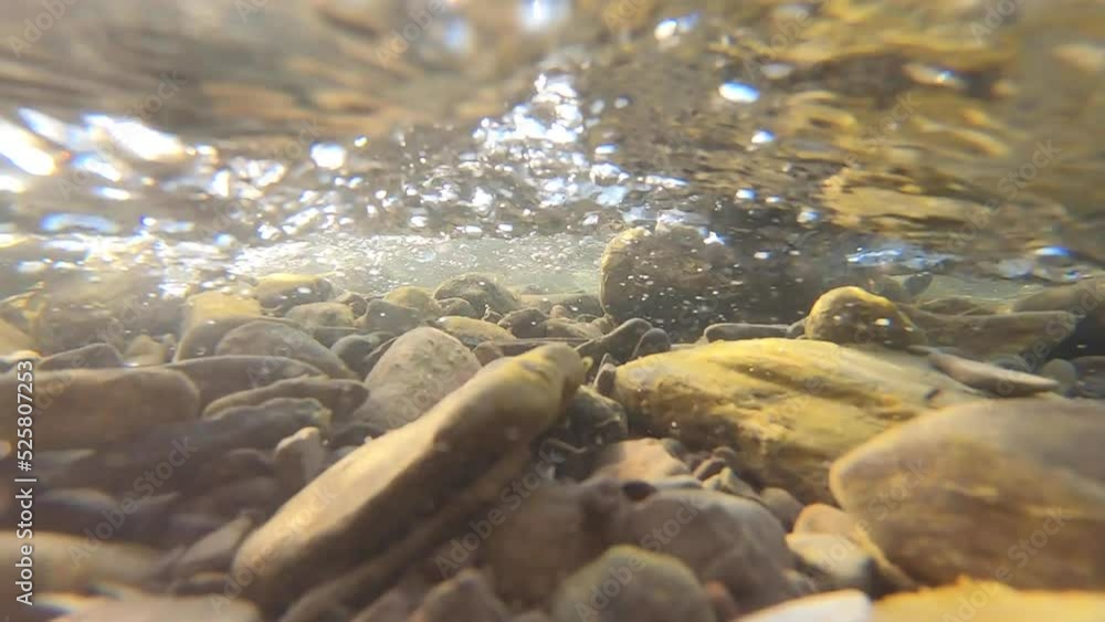 Flow of water in mountain river. View inside from below. Flowing water, mud-covered rocks stones at bottom of river and water bubbles clopse-up. Sun glare Underwater view. Beautiful natural background Flow of water in mountain river. View inside from below. Flowing water, mud-covered rocks stones at bottom of river and water bubbles clopse-up. Sun glare Underwater view. Beautiful natural background