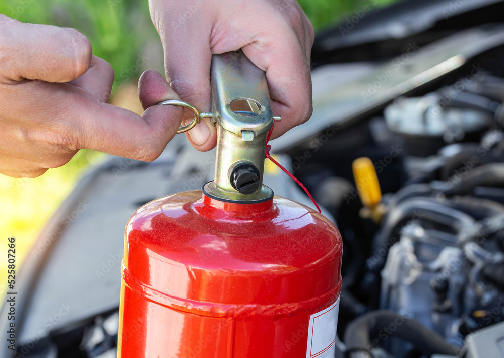 Naklejka premium A man takes out a pin from a car fire extinguisher. The concept of the expiration date of a fire extinguisher, extinguishing a fire. Close-up
