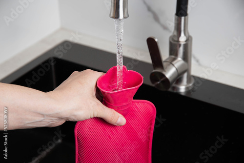 A woman pours hot water into a medical heating pad from the tap. Treatment of diseases with heat, close-up