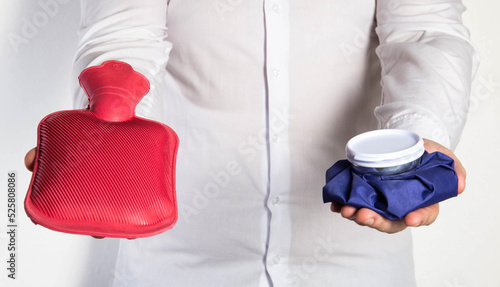 A man in a white shirt holds an ice bag and a red medical heating pad for hot water. The concept of heat and cold treatment. First aid for pain and inflammation photo