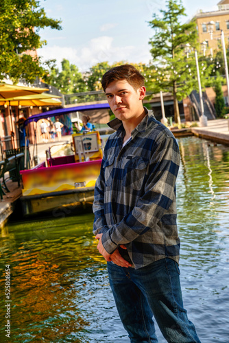 Handsome young man standing by a canal with the sun to his back and a confident expression.