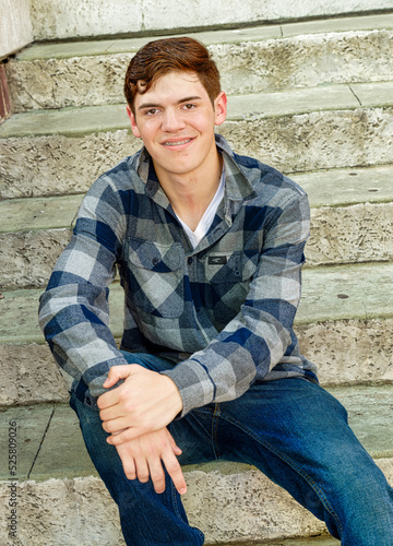 Handsome young man sitting by cement stairs and confidently smiling.