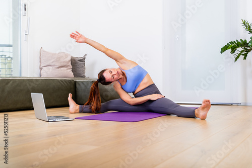 Beautiful and athletic fit girl doing stratching at home at loft studio, using laptop