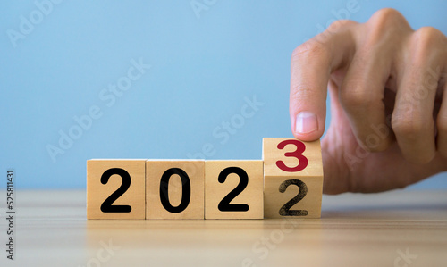 Man hands flipping of 2022 to 2023 on wooden block cube.happy new year 2023.Teble and blue background.