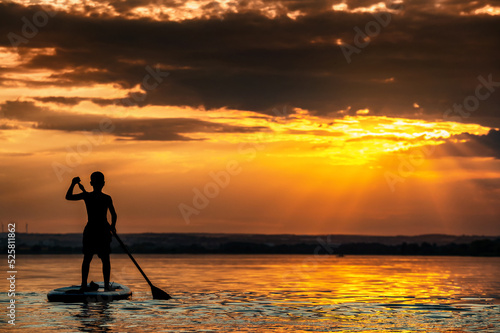 Sonne spiegelt sich im Wasser eines See während ein Kind auf einem Stand Up Paddle fährt