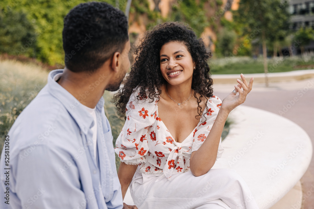 Positive young african friends chat spending time outdoors during day. Brunette girl and guy are wearing summer clothes. Modern lifestyle, people and youth concept Positive young african friends chat spending time outdoors during day. Brunette girl and guy are wearing summer clothes. Modern lifestyle, people and youth concept