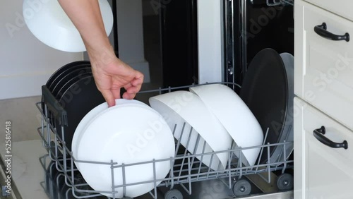 Woman hand taking clean plates from the basket of automatic stainless built-in dishwasher machine with clean utensils inside in modern home kitchen. Household domestic life. Full HD Footage