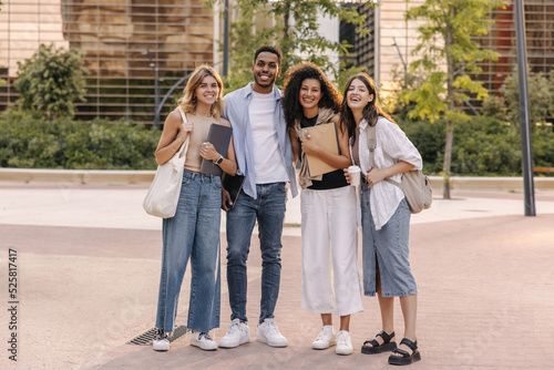 Full length happy young interracial students spend time outdoors outside college. Guy and girls look at camera, wear summer clothes. Lifestyle concept