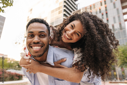 Smiling african young girl and her boyfriend are looking at camera having fun together. Couple of lovers stand in embrace on street. Good mood concept
