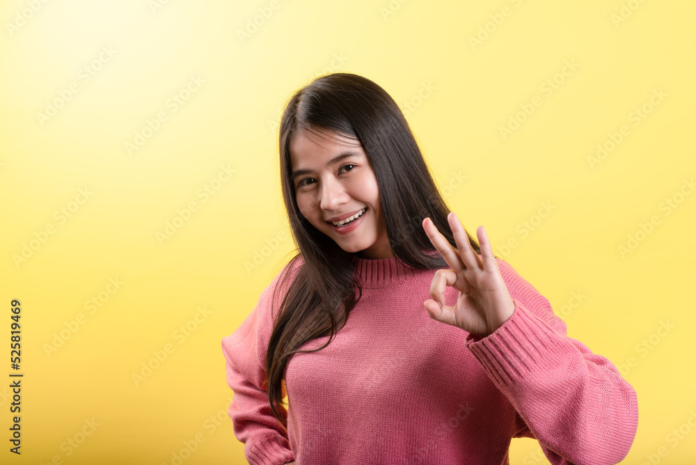 Obraz premium Portrait of a beautiful Asian businesswoman smiling and showing a falling sign on a yellow background. Looking at the camera.