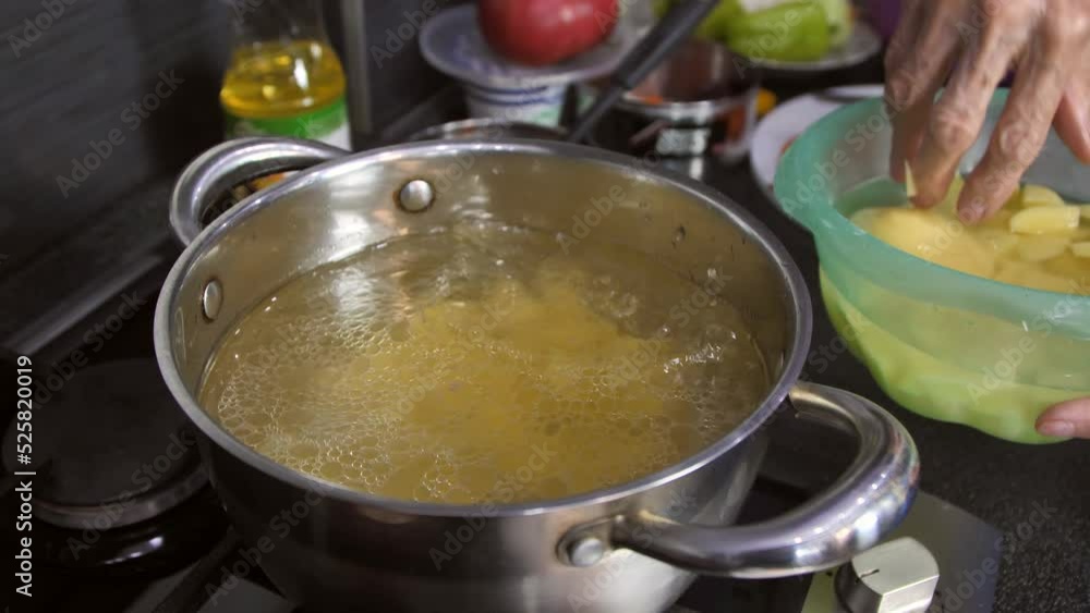 hands of an old woman put raw chopped potatoes for soup into a pot of broth hands of an old woman put raw chopped potatoes for soup into a pot of broth