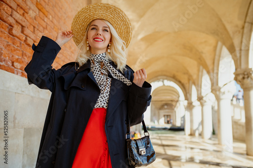 Happy smiling fashionable woman wearing straw hat, polka dot blouse, red skirt, holding handbag, posing in street of Venice. Fashion, travel, lifestyle conception. Copy, empty space for text