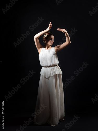 An ancient heroine, a young woman in the image of an ancient Greek goddess or muse. A noble heroine in a white tunic and a laurel wreath, dancing on a black background