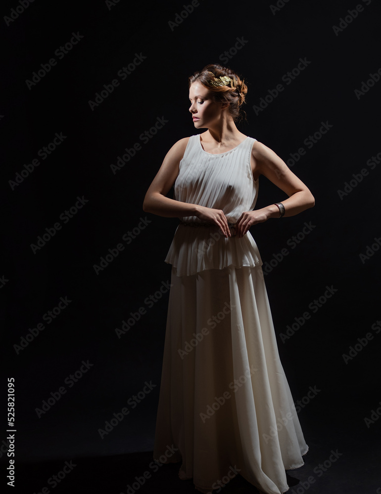 An ancient heroine, a young woman in the image of an ancient Greek goddess or muse. A noble heroine in a white tunic and a laurel wreath, a full-length photo on a black background