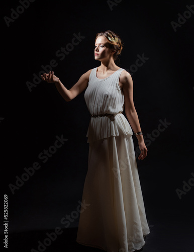 An ancient heroine  a young woman in the image of an ancient Greek goddess or muse. A noble heroine in a white tunic and a laurel wreath  a full-length photo on a black background