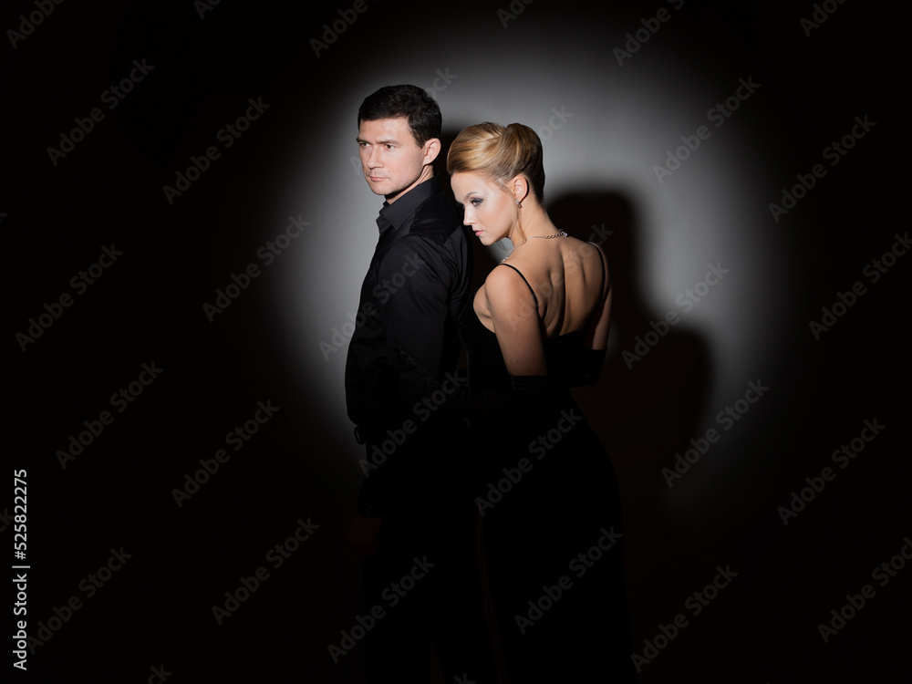 An attractive couple in black. Stylish and elegant young man and woman in the spotlight. Beautiful blonde in a long dress and a guy in a black shirt,