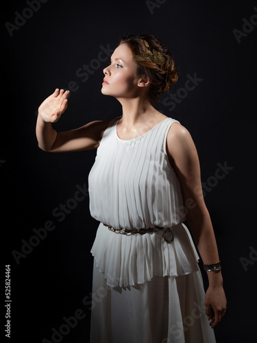An ancient heroine, a young woman in the image of an ancient Greek goddess or muse. A noble heroine in a white tunic and a laurel wreath, dancing on a black background