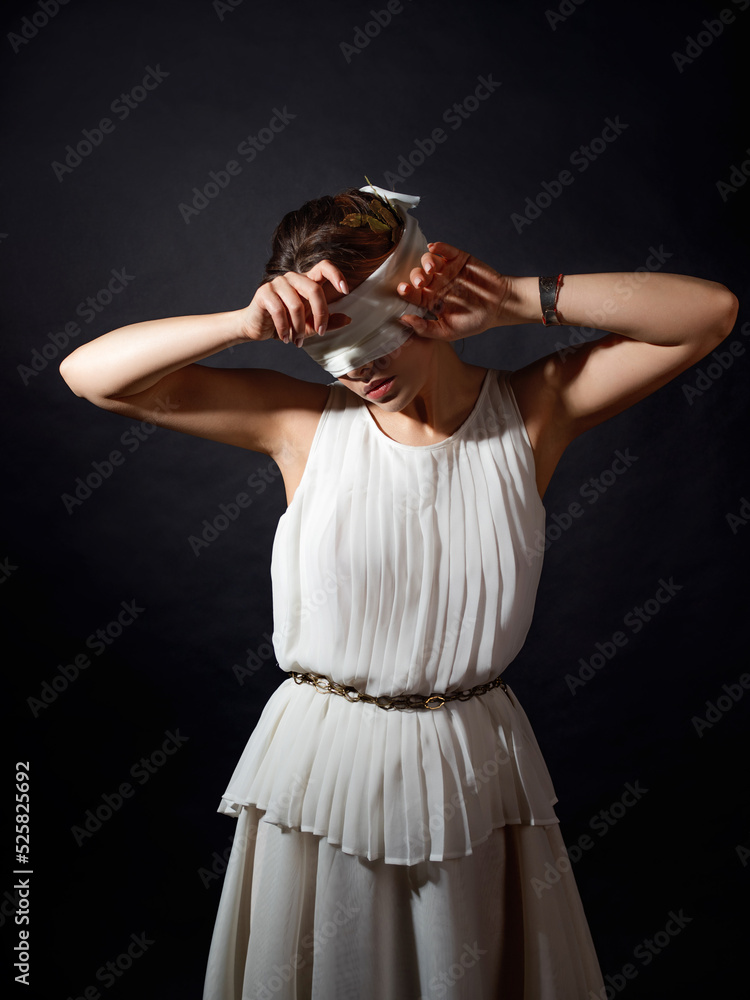 Close your eyes, hide from the truth, concept. An ancient heroine blindfolded, a young woman in a tunic with a blindfold, covers her face with her hands Close your eyes, hide from the truth, concept. An ancient heroine blindfolded, a young woman in a tunic with a blindfold, covers her face with her hands