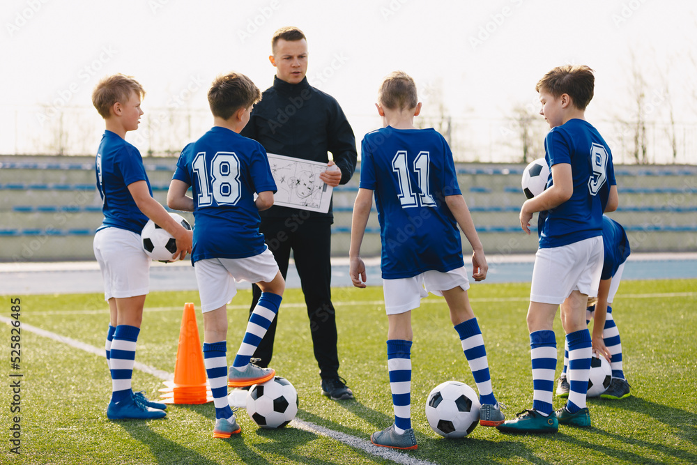 Obraz premium Football coach coaching children. Young coach teaching kids on football field. Trainer explains to schoolboys training rules. Soccer football training session for children. Football tactic education.