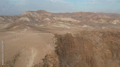 Man walking on a cliff in a desert landscape.