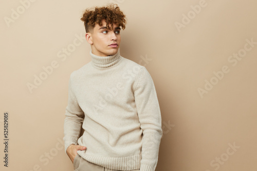 a handsome, attractive man stands on a beige background in stylish clothes and poses relaxed looking at the camera