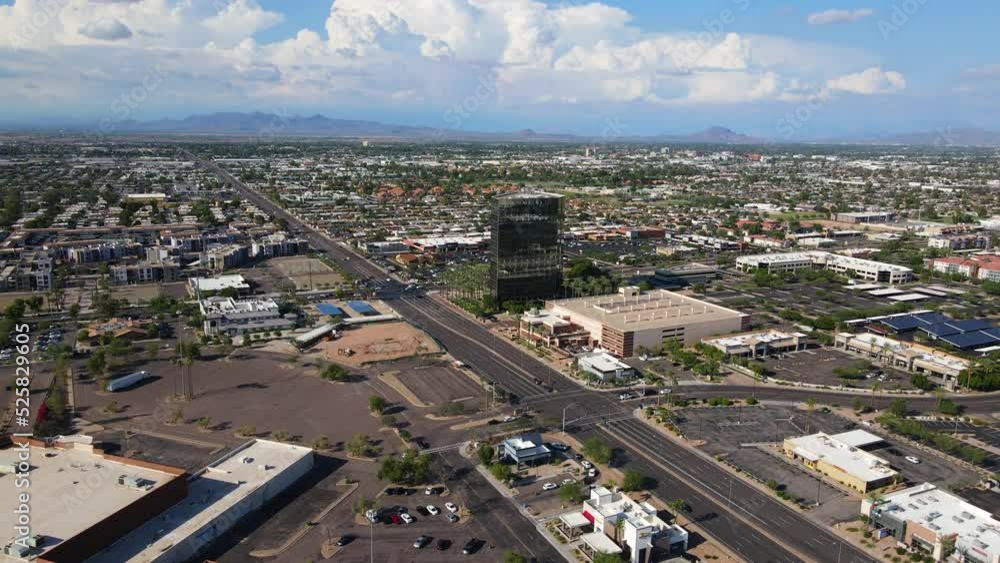 4K Drone flying toward a small skyscraper in Mesa Arizona surrounded by palm trees , mountains in the background, and large cumulonimbus clouds in the sky