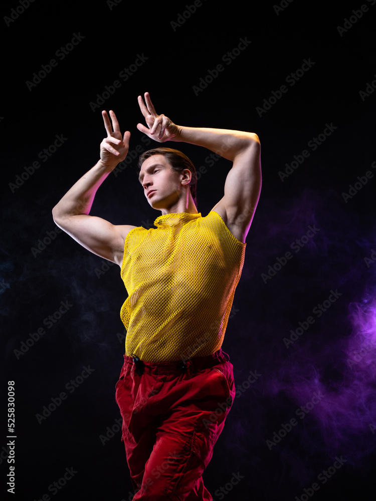 a young muscular man in a bright outfit poses in a pretentious pose, style and grotesque. An attractive guy with pumped-up arms in a mesh T-shirt on a naked body a young muscular man in a bright outfit poses in a pretentious pose, style and grotesque. An attractive guy with pumped-up arms in a mesh T-shirt on a naked body