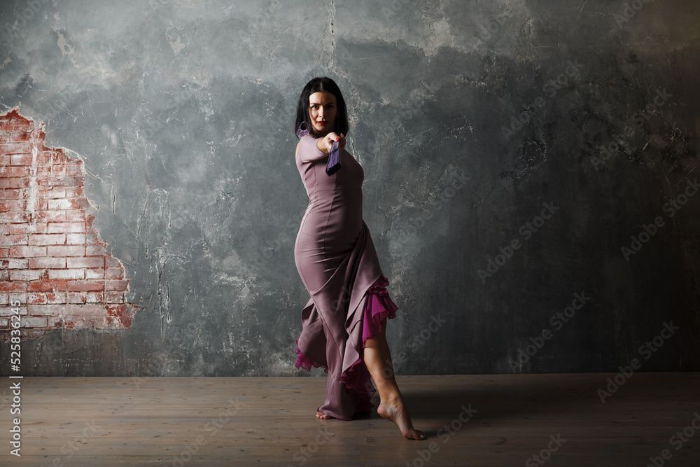 Fototapeta premium Young adult spanish woman dancing flamenco on gray vintage studio background
