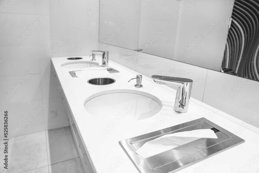 Fototapeta premium White sinks with paper towels, urns, soap and automatic faucets in a public restroom