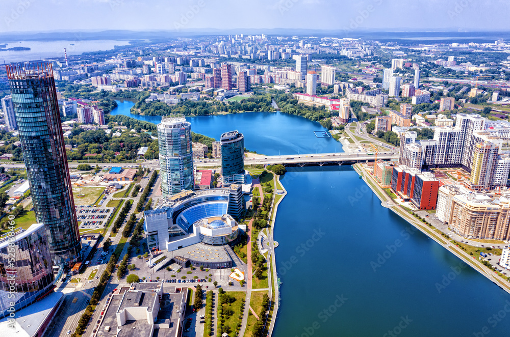 Aerial view of central part of modern city with skyscrapers and residential buildings. River and bridge on summer day. Yekaterinburg. Russia