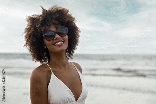 Portrait of beautiful smiling black woman with curly hair wearing sunglasses on the beach.