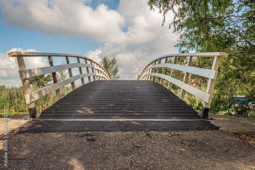 Simple wooden bridge with white bridge railings contrasting with the sky. The photo was taken on a sunny day in the summer in the Dutch province of South Holland.