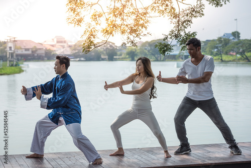 Group of young people practicing traditional Tai Chi Chuan, Tai Ji and Qi Gong for fighting match together in the park on the lake background, traditional chinese martial arts concept.