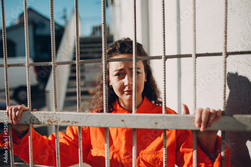 Canvas Print Young brunette curly woman in orange suit behind cage