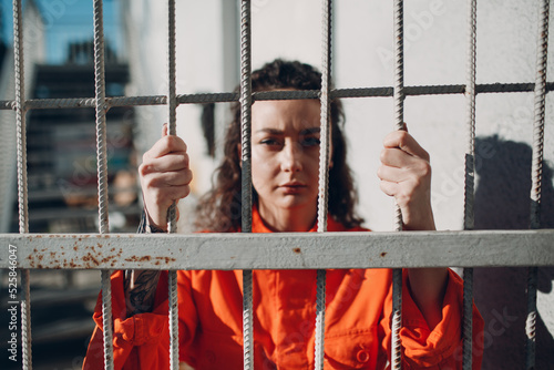 Fotótapéta Young woman in orange suit behind jail bars